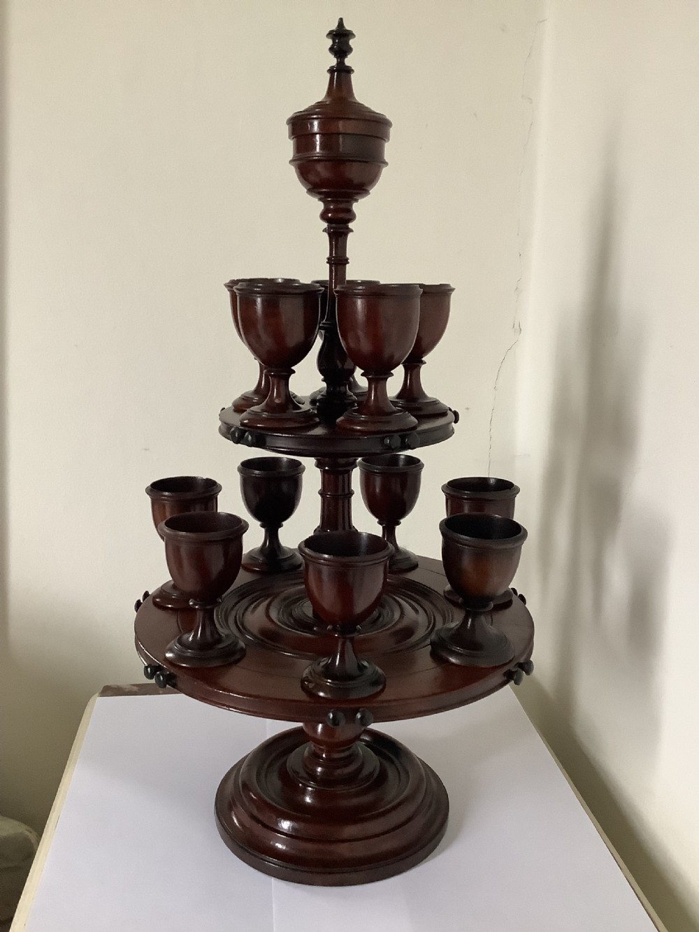 A dark turned mahogany two-tier revolving egg cup stand with a central finial and matching wooden egg cups.