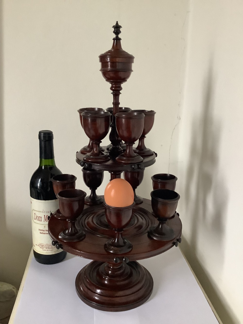 A dark turned mahogany two-tier revolving egg cup stand with a central finial and matching wooden egg cups. View II