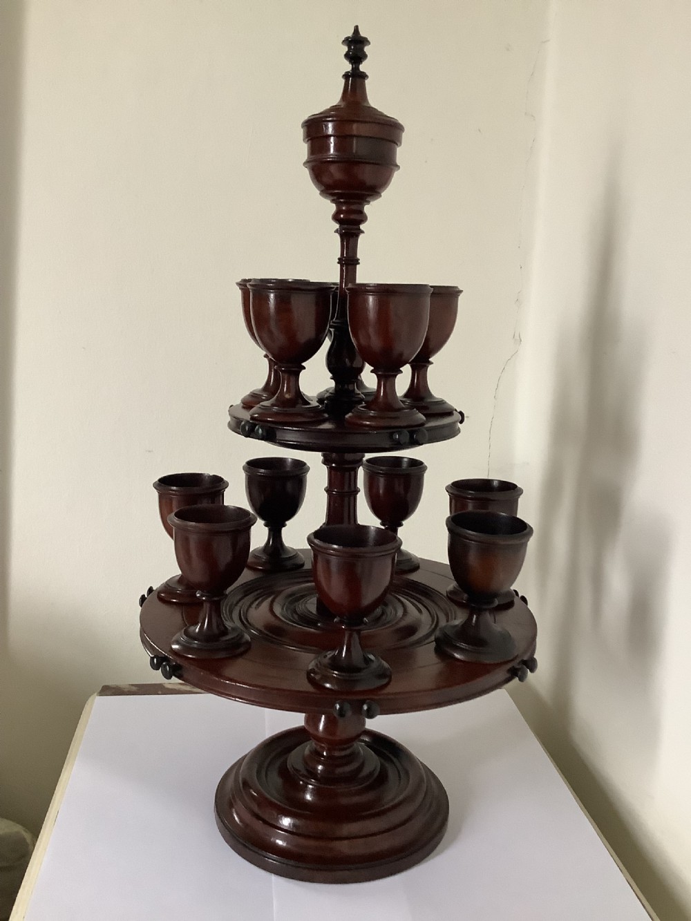 A dark turned mahogany two-tier revolving egg cup stand with a central finial and matching wooden egg cups. View IV
