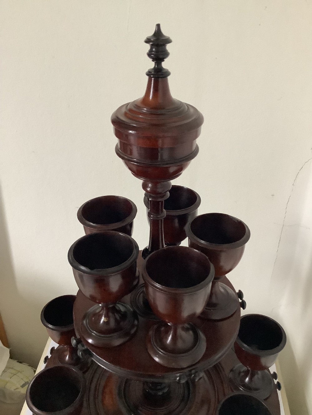 A dark turned mahogany two-tier revolving egg cup stand with a central finial and matching wooden egg cups. View V