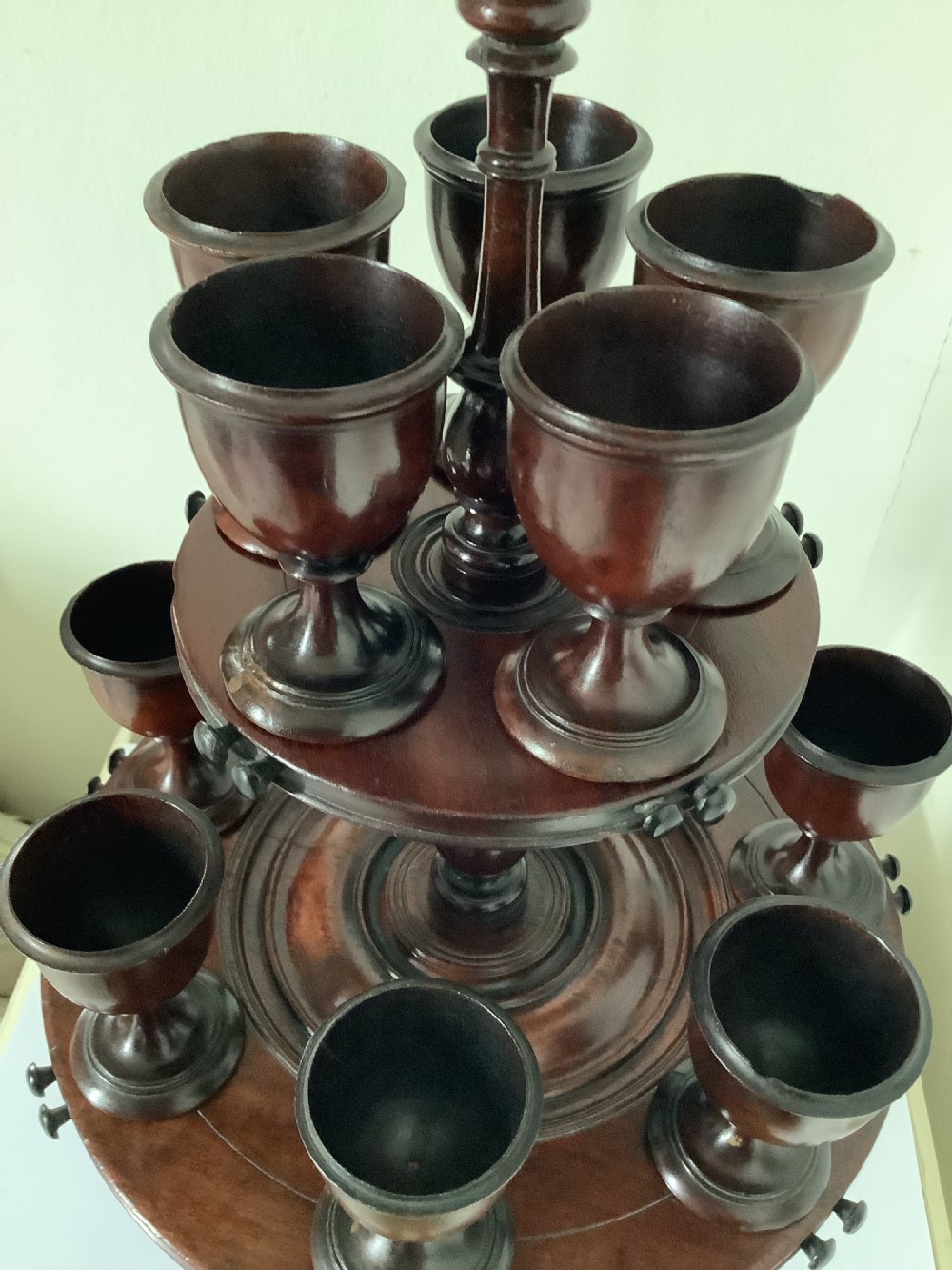 A dark turned mahogany two-tier revolving egg cup stand with a central finial and matching wooden egg cups. View VI
