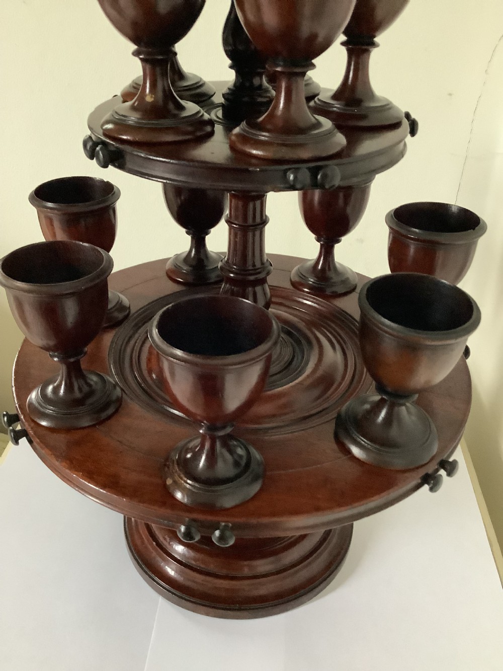 A dark turned mahogany two-tier revolving egg cup stand with a central finial and matching wooden egg cups. View VII