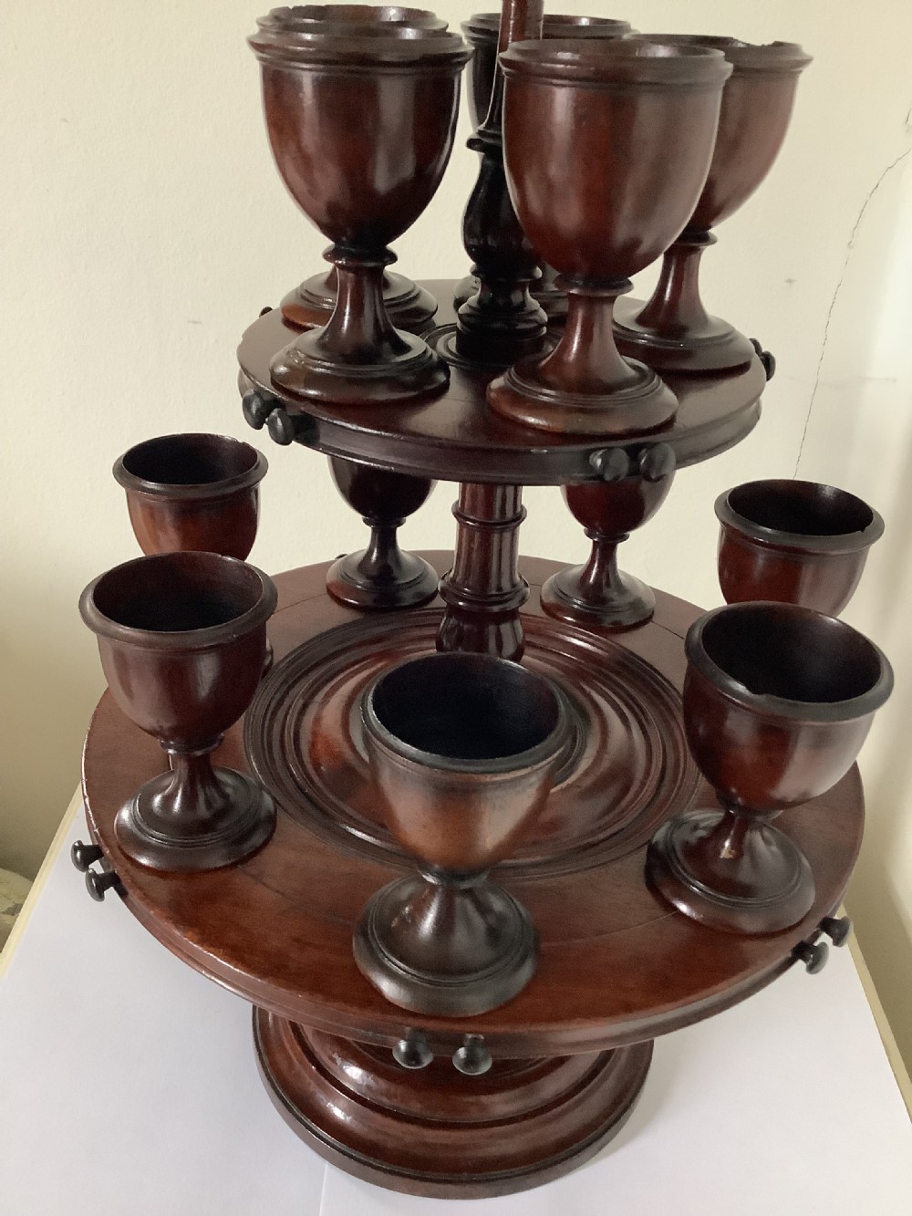 A dark turned mahogany two-tier revolving egg cup stand with a central finial and matching wooden egg cups. View VIII