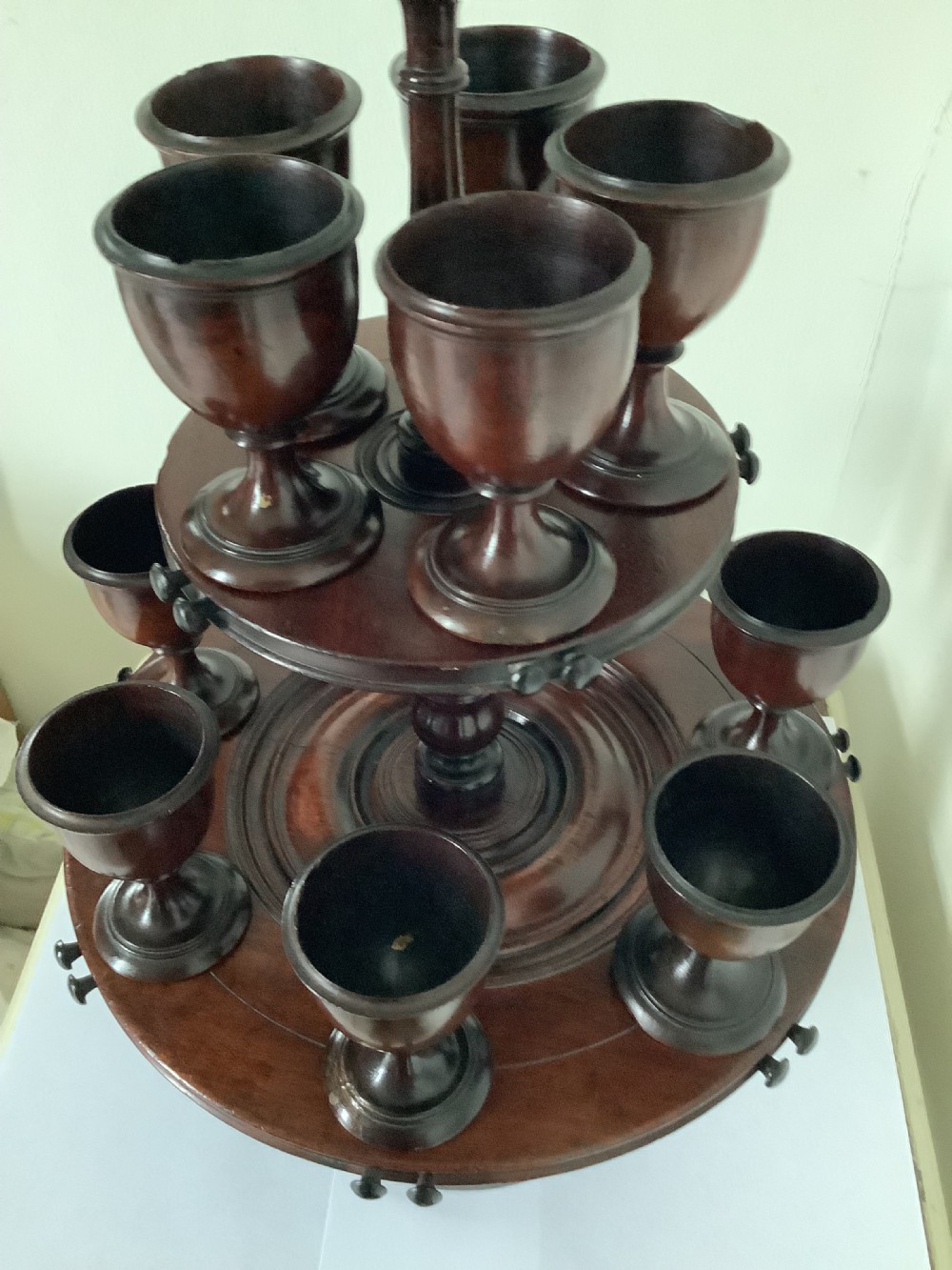 A dark turned mahogany two-tier revolving egg cup stand with a central finial and matching wooden egg cups. View X