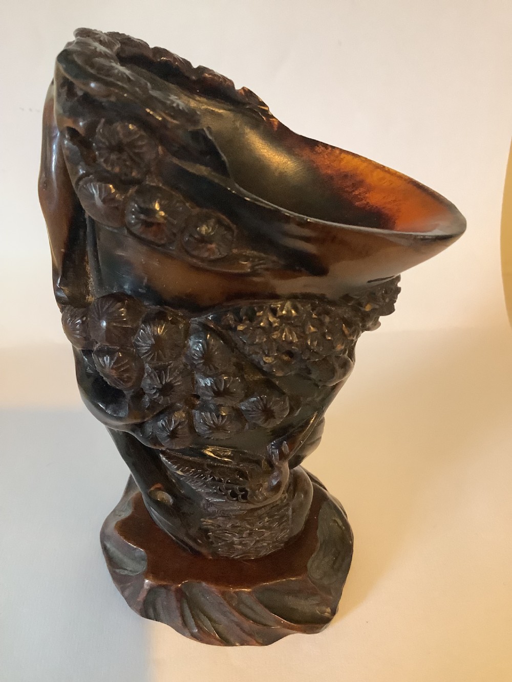 A deeply carved dark brown Chinese horn libation cup featuring intricate figural and floral relief details. View III