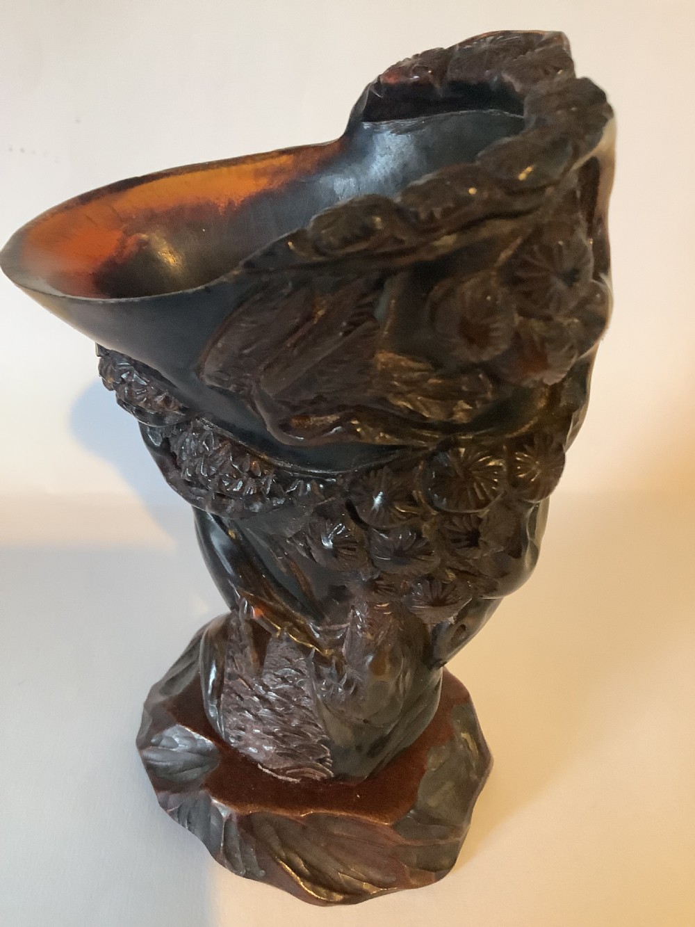 A deeply carved dark brown Chinese horn libation cup featuring intricate figural and floral relief details. View II