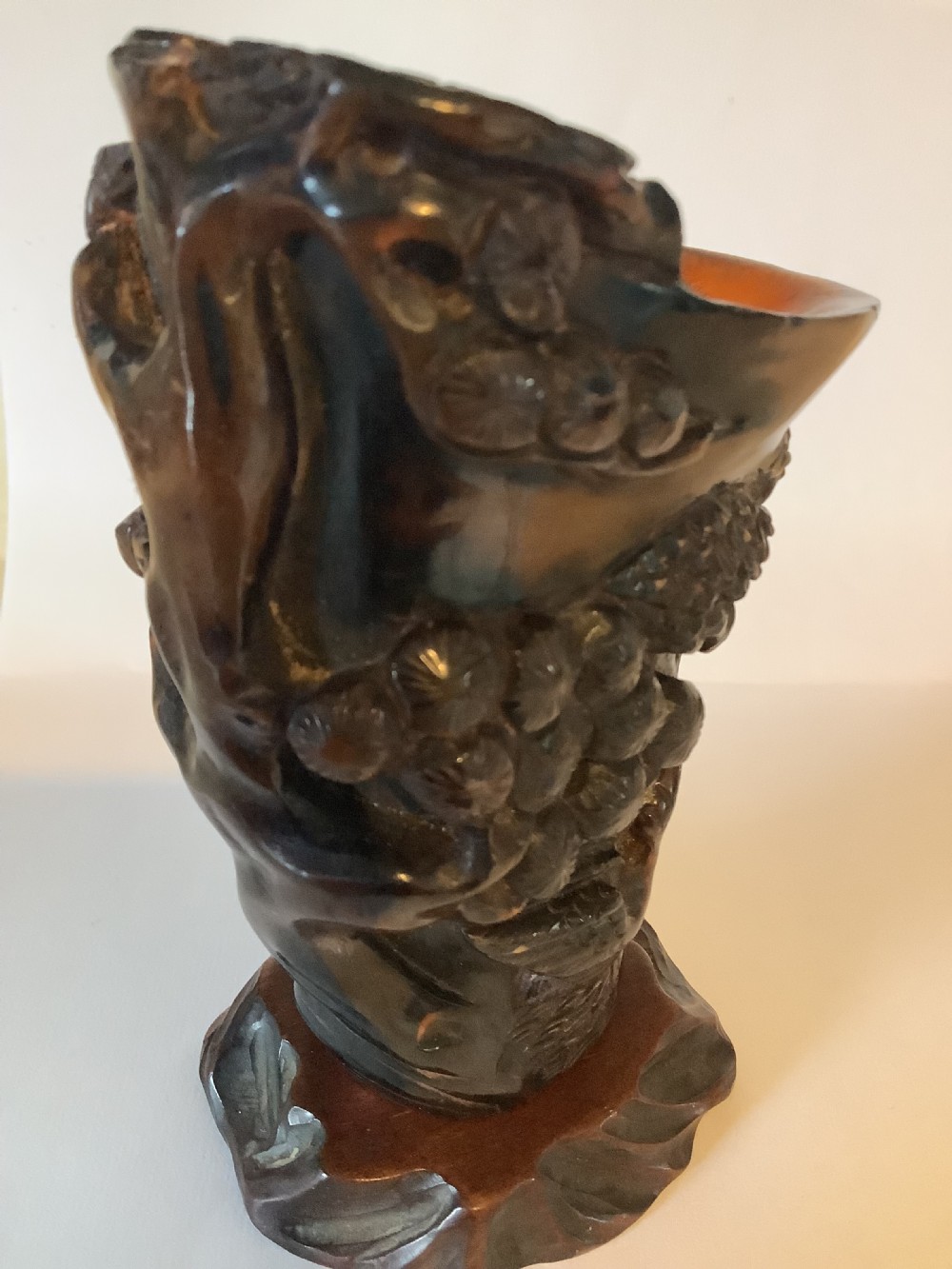 A deeply carved dark brown Chinese horn libation cup featuring intricate figural and floral relief details. View V