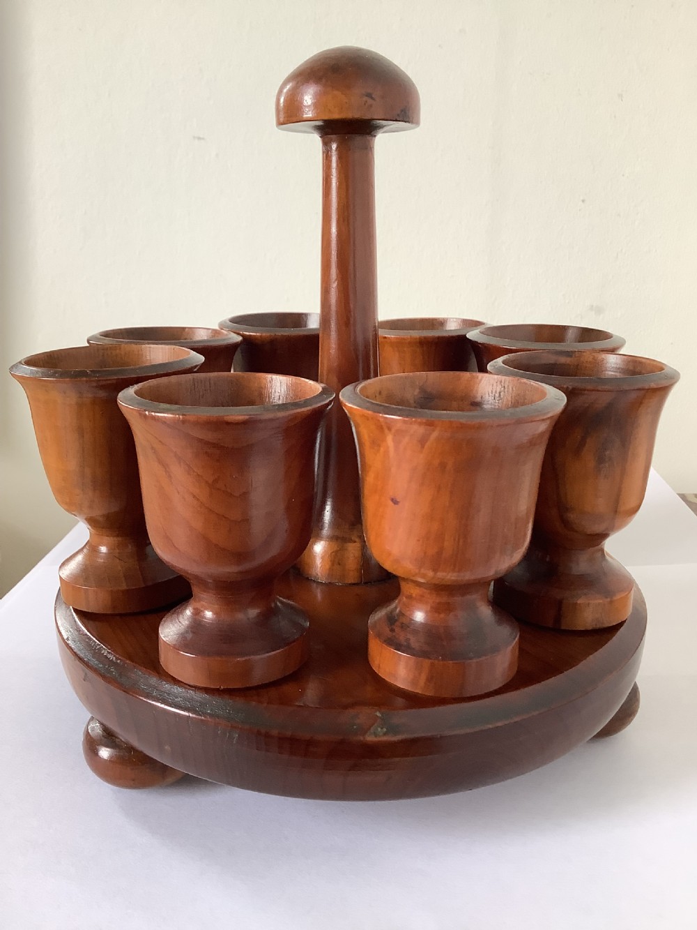 A turned yew wood circular eggcup stand featuring a central carrying handle surrounded by eight turned wooden eggcups on a circular base supported by small bun feet.