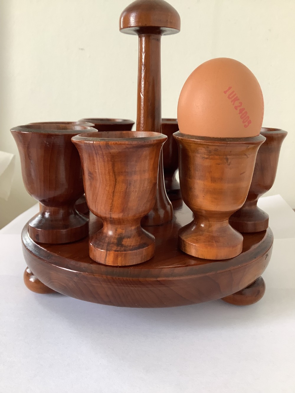 A turned yew wood circular eggcup stand featuring a central carrying handle surrounded by eight turned wooden eggcups on a circular base supported by small bun feet. View II