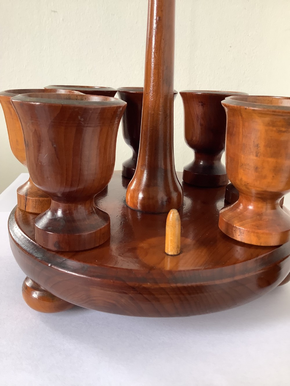 A turned yew wood circular eggcup stand featuring a central carrying handle surrounded by eight turned wooden eggcups on a circular base supported by small bun feet. View III