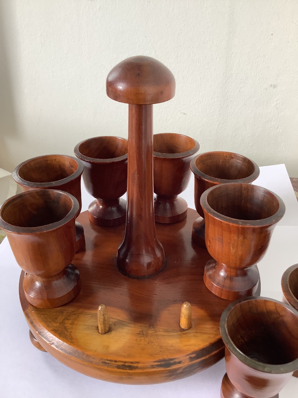 A turned yew wood circular eggcup stand featuring a central carrying handle surrounded by eight turned wooden eggcups on a circular base supported by small bun feet. View IV