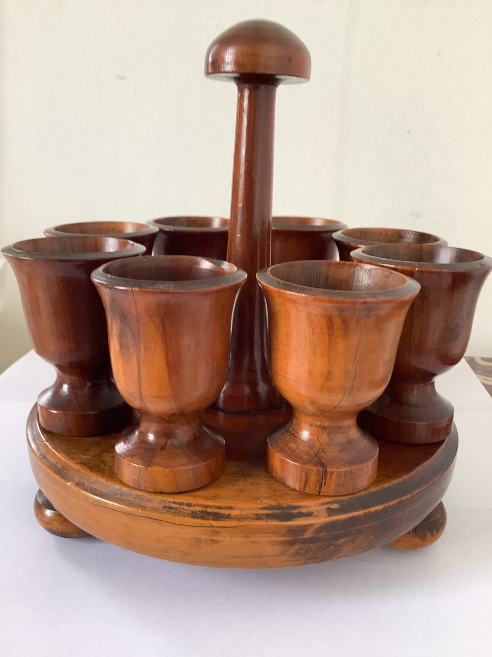 A turned yew wood circular eggcup stand featuring a central carrying handle surrounded by eight turned wooden eggcups on a circular base supported by small bun feet. View V