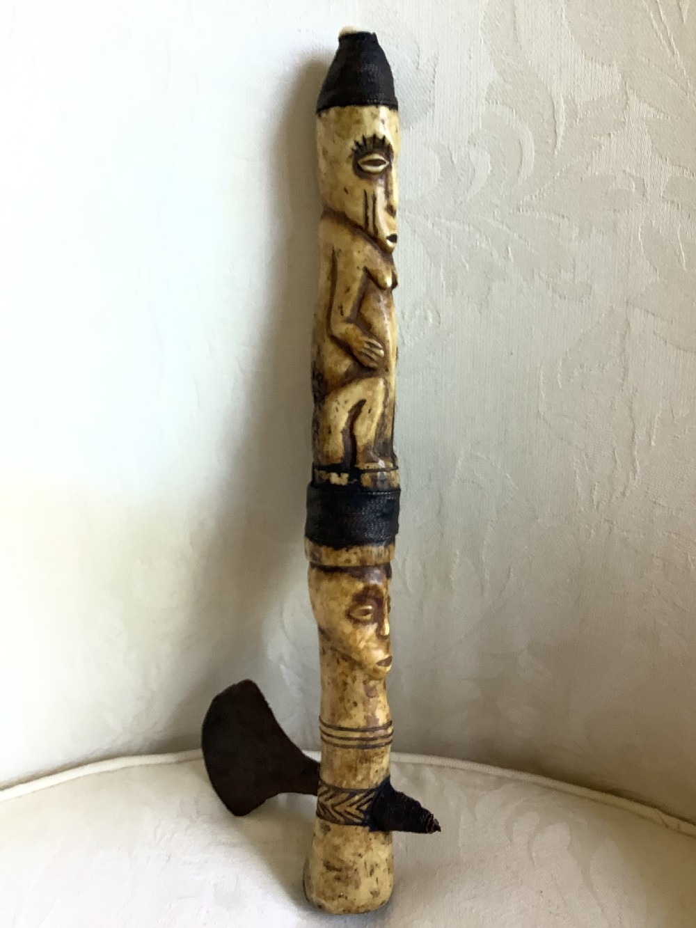A carved bone ceremonial axe featuring stacked figurative human carvings along the shaft and a small dark iron blade fixed near the base.
