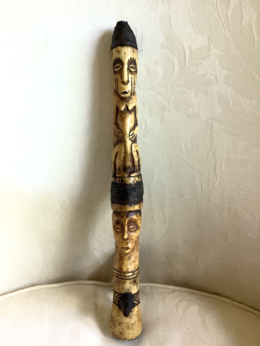 A carved bone ceremonial axe featuring stacked figurative human carvings along the shaft and a small dark iron blade fixed near the base. View III