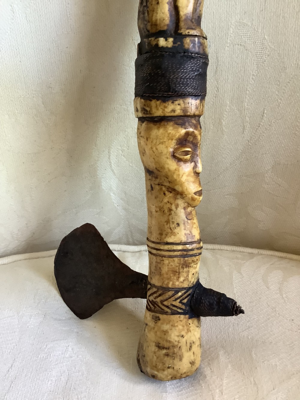 A carved bone ceremonial axe featuring stacked figurative human carvings along the shaft and a small dark iron blade fixed near the base. View IV