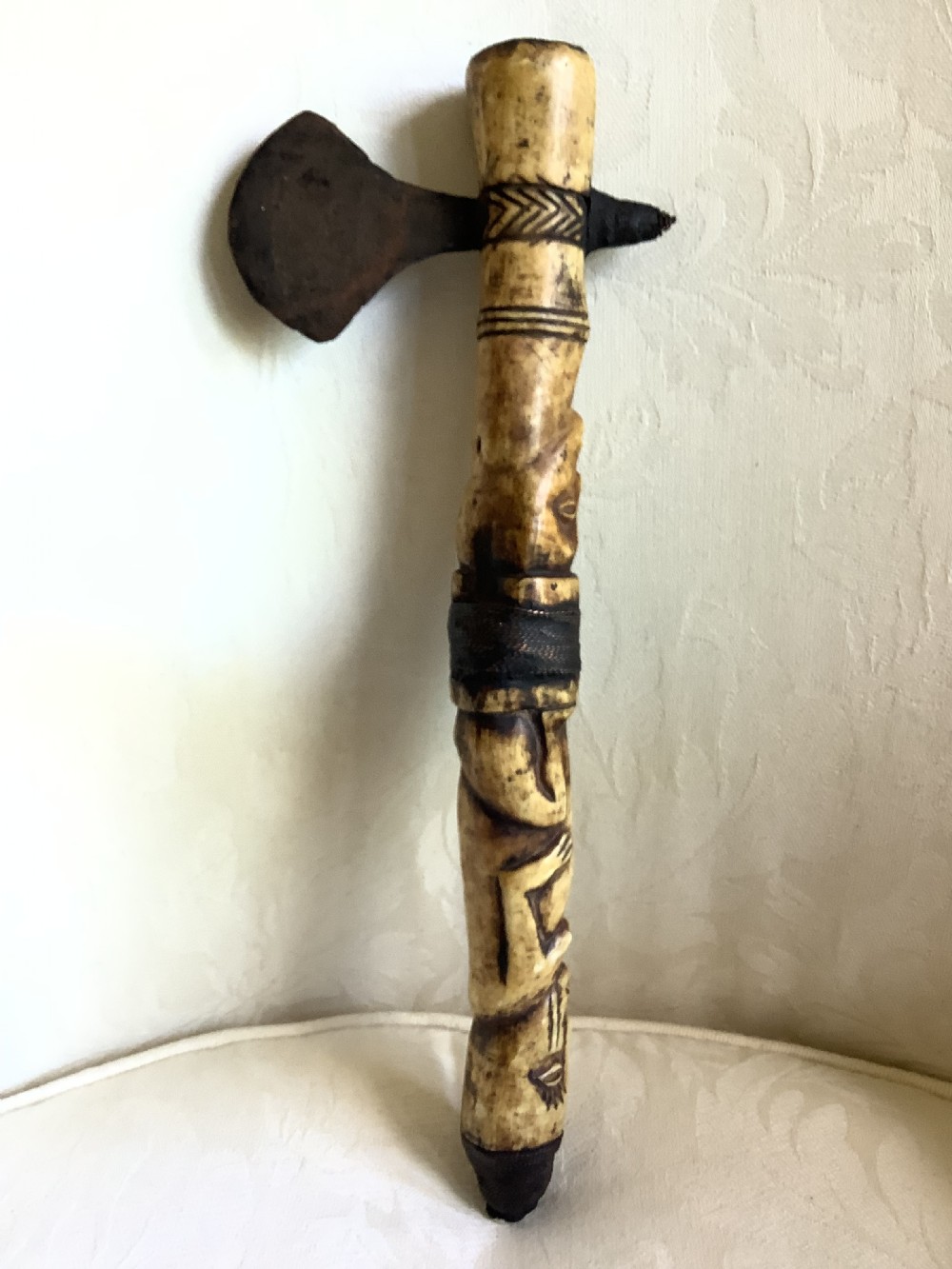 A carved bone ceremonial axe featuring stacked figurative human carvings along the shaft and a small dark iron blade fixed near the base. View V