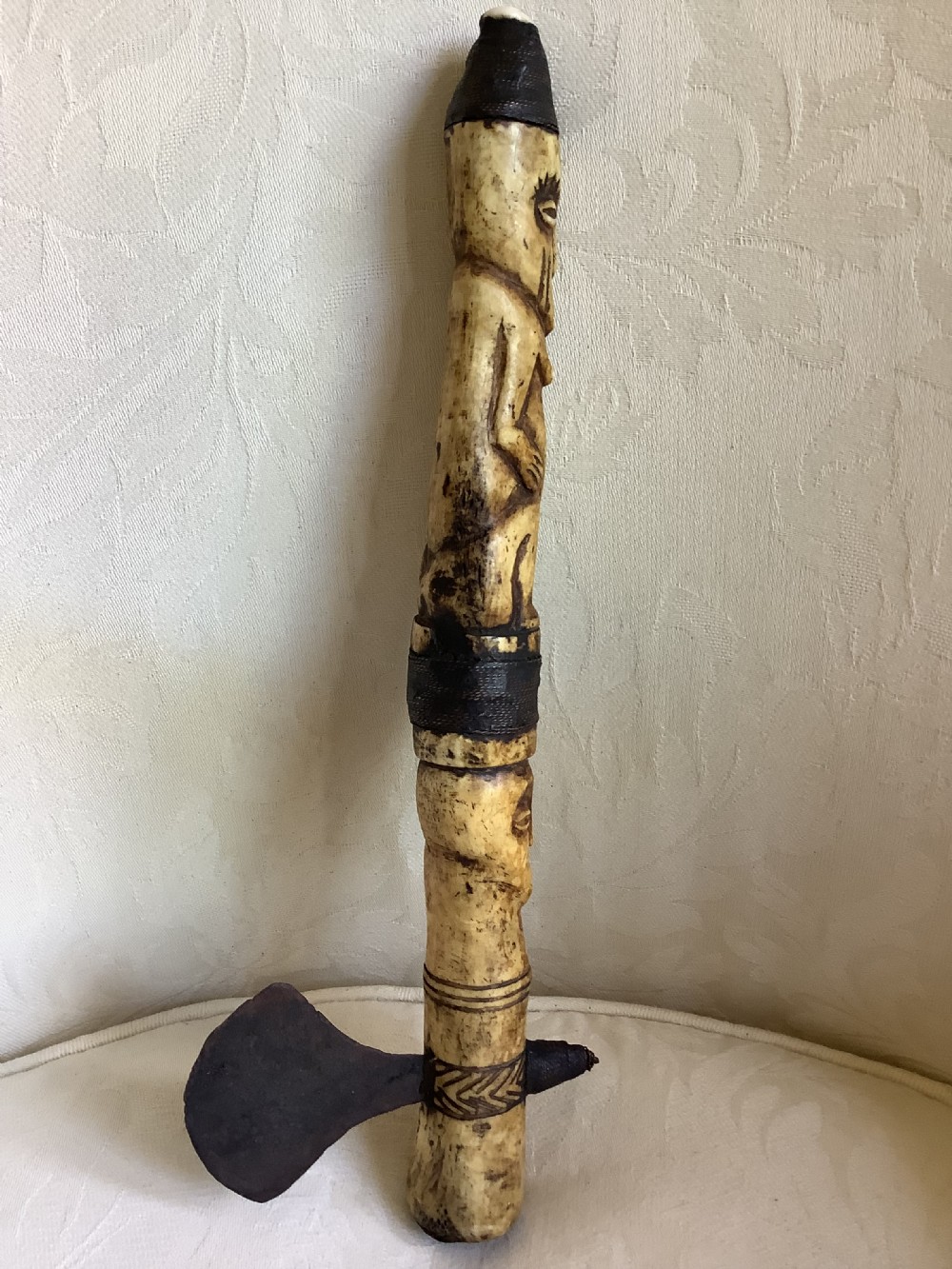 A carved bone ceremonial axe featuring stacked figurative human carvings along the shaft and a small dark iron blade fixed near the base. View VI