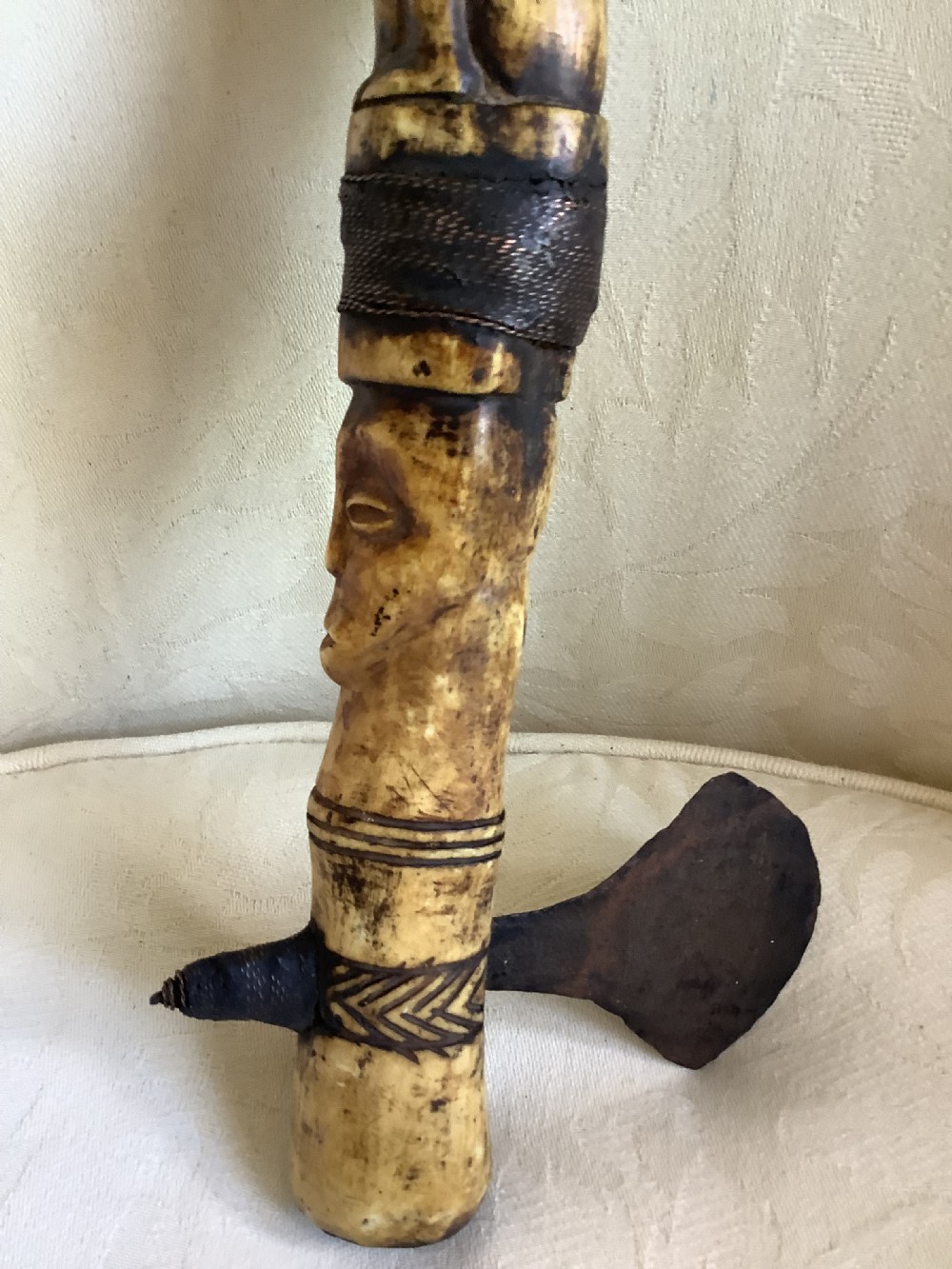 A carved bone ceremonial axe featuring stacked figurative human carvings along the shaft and a small dark iron blade fixed near the base. View VIII