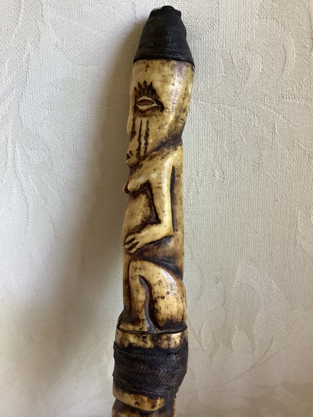 A carved bone ceremonial axe featuring stacked figurative human carvings along the shaft and a small dark iron blade fixed near the base. View IX