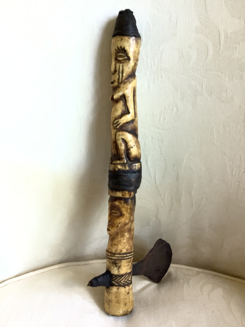 A carved bone ceremonial axe featuring stacked figurative human carvings along the shaft and a small dark iron blade fixed near the base. View X