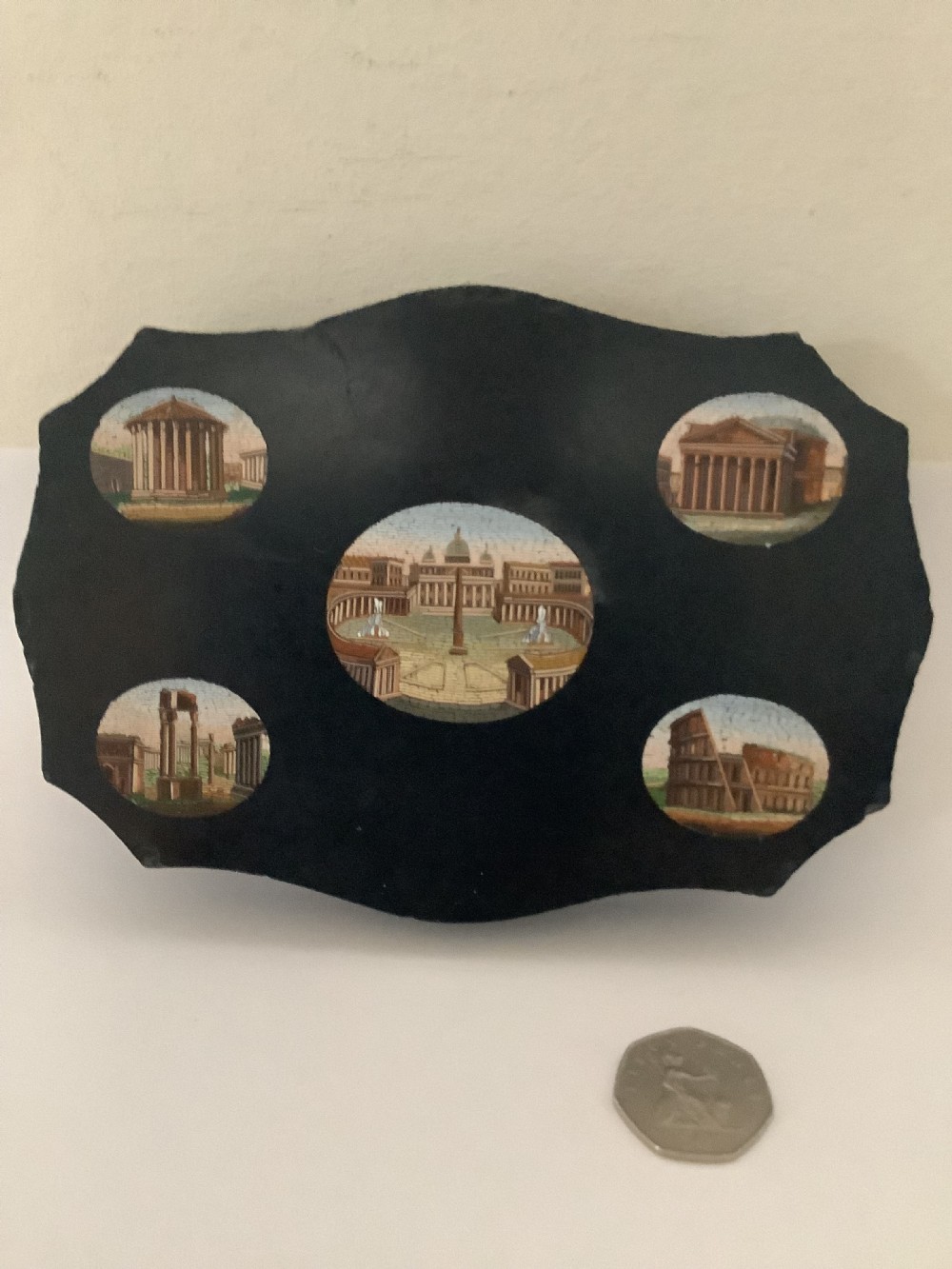 A shaped black marble plaque inlaid with five detailed micromosaic panels depicting classical Roman landmarks including Saint Peters Square and the Colosseum.