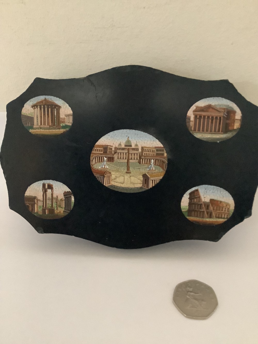A shaped black marble plaque inlaid with five detailed micromosaic panels depicting classical Roman landmarks including Saint Peters Square and the Colosseum. View II