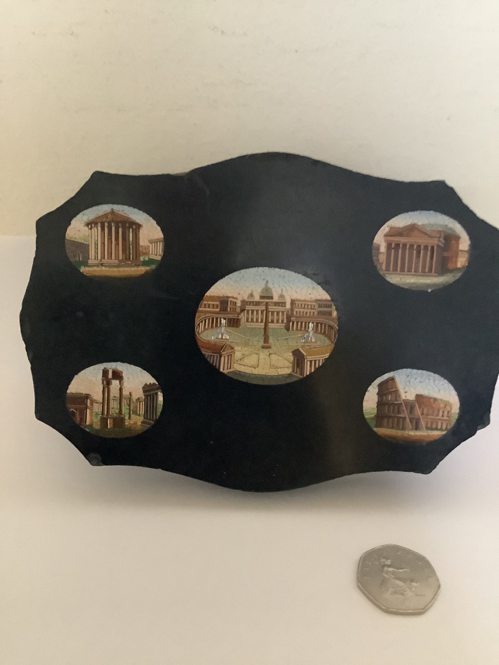 A shaped black marble plaque inlaid with five detailed micromosaic panels depicting classical Roman landmarks including Saint Peters Square and the Colosseum. View III