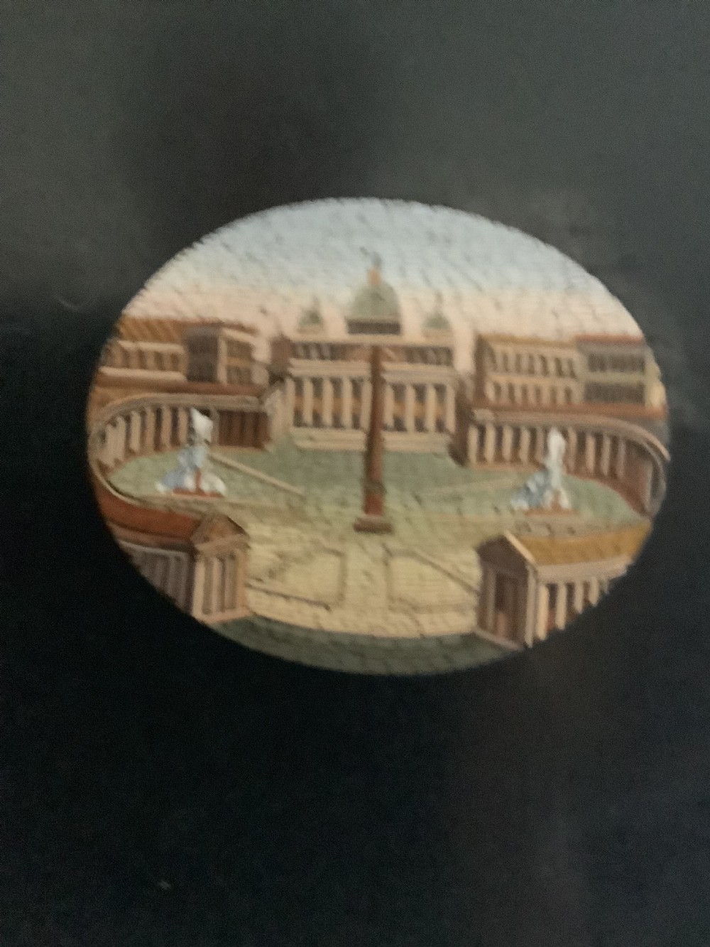 A shaped black marble plaque inlaid with five detailed micromosaic panels depicting classical Roman landmarks including Saint Peters Square and the Colosseum. View V