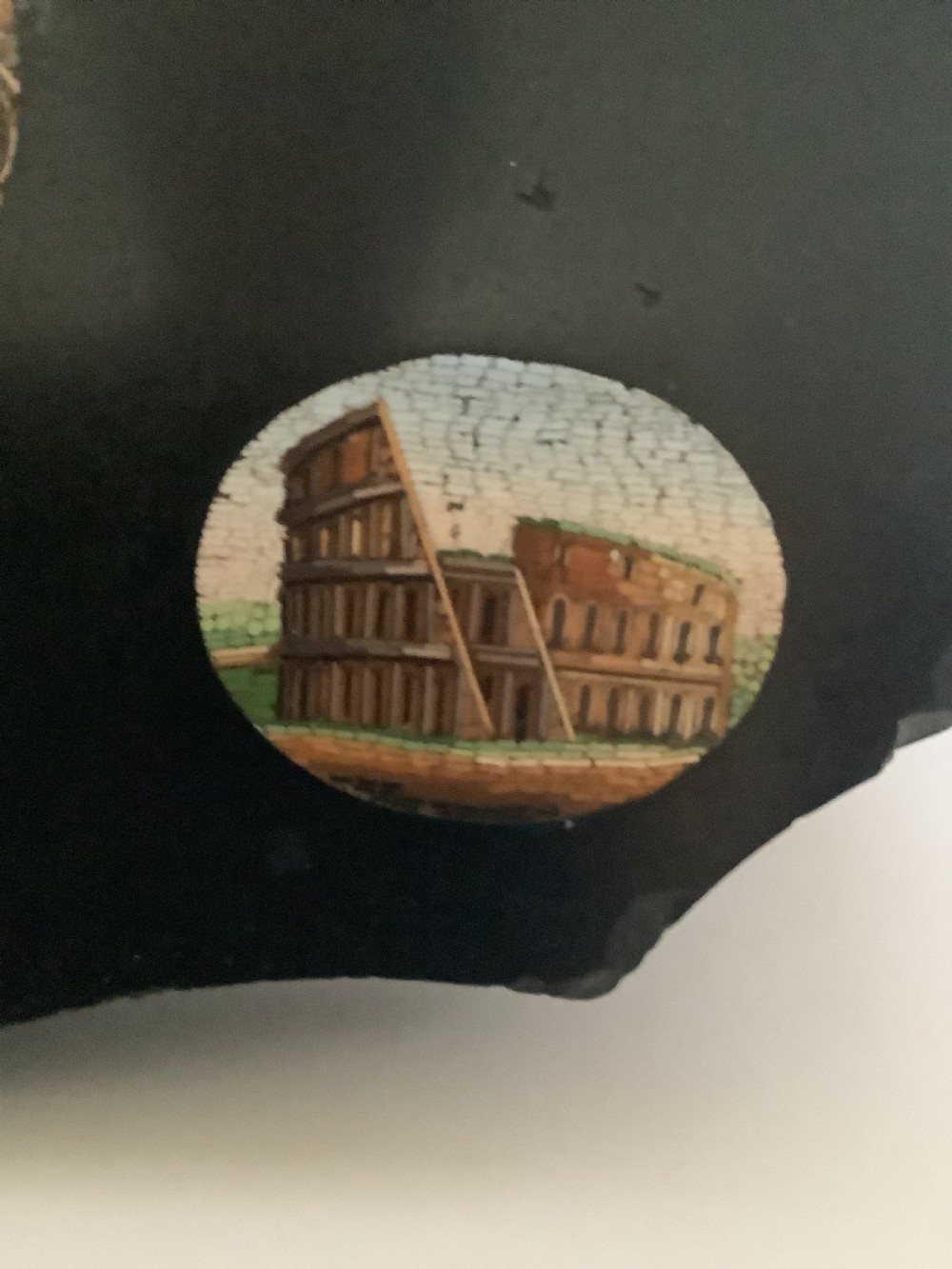 A shaped black marble plaque inlaid with five detailed micromosaic panels depicting classical Roman landmarks including Saint Peters Square and the Colosseum. View VII