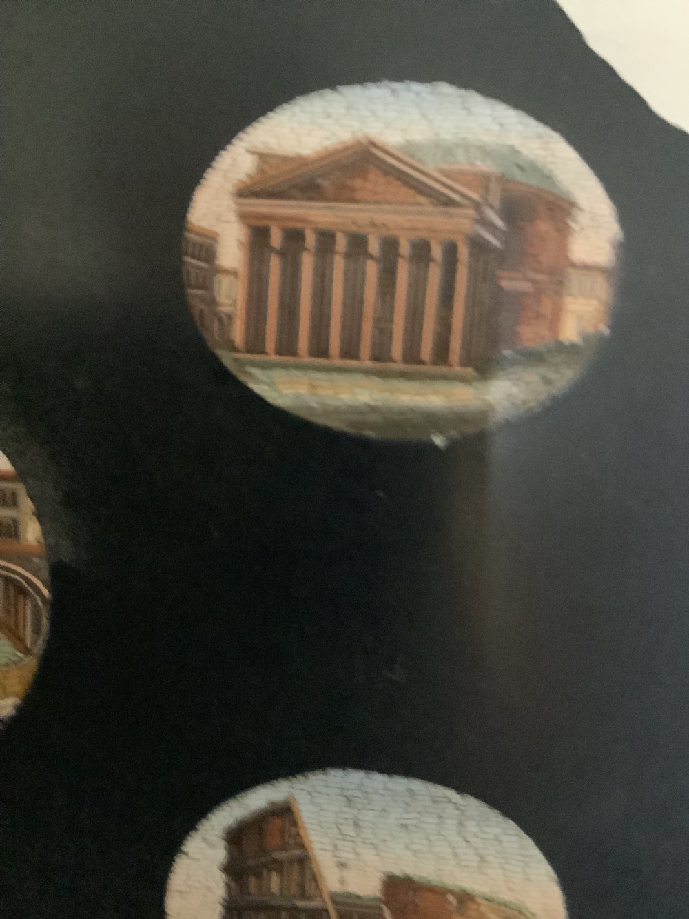 A shaped black marble plaque inlaid with five detailed micromosaic panels depicting classical Roman landmarks including Saint Peters Square and the Colosseum. View VIII