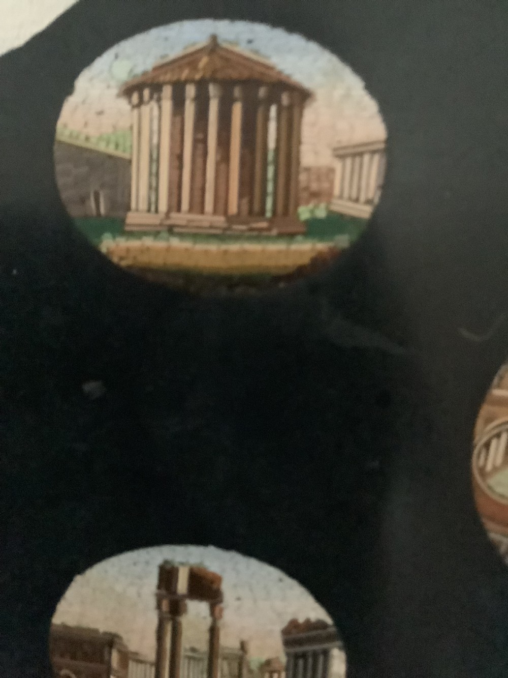 A shaped black marble plaque inlaid with five detailed micromosaic panels depicting classical Roman landmarks including Saint Peters Square and the Colosseum. View IX