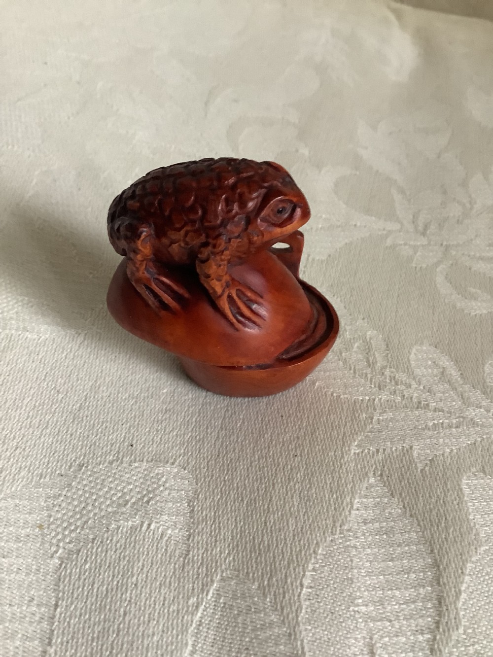 A dark brown carved wood netsuke shaped as a textured toad resting on a curved base. View III