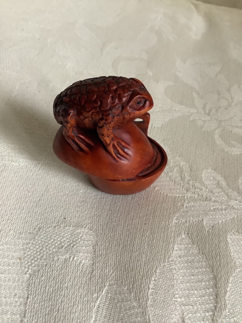 A dark brown carved wood netsuke shaped as a textured toad resting on a curved base.