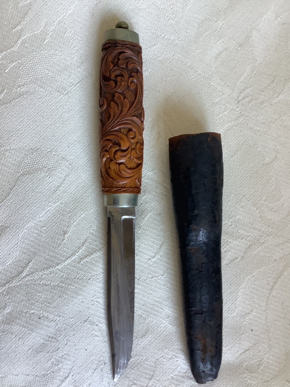 An antique Norwegian dagger featuring a carved wooden handle with acanthus leaf motifs, a steel blade, and an accompanying dark leather sheath. View II