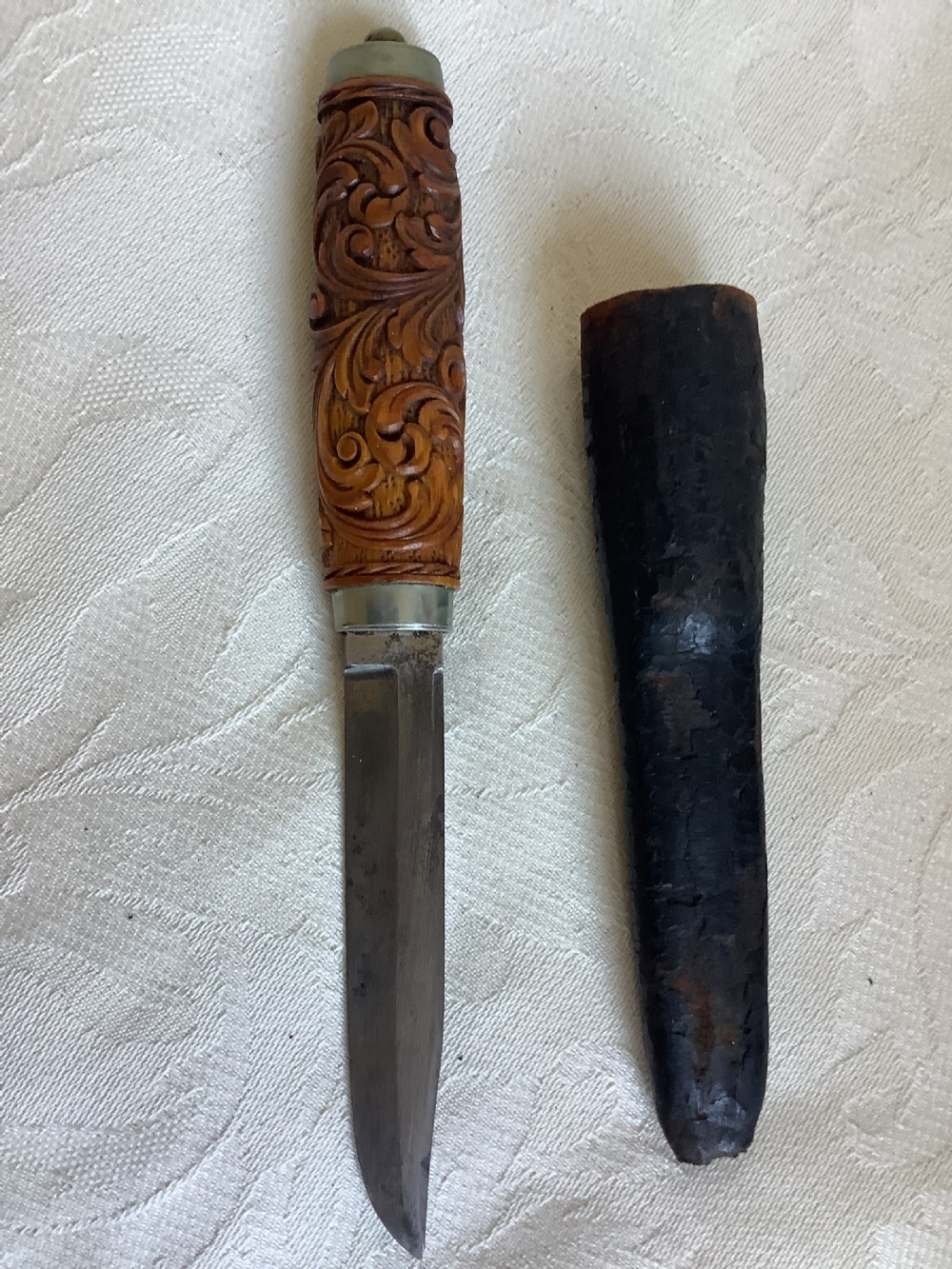 An antique Norwegian dagger featuring a carved wooden handle with acanthus leaf motifs, a steel blade, and an accompanying dark leather sheath. View VI