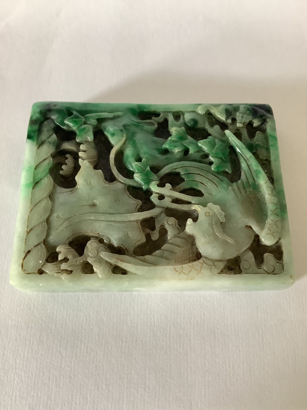 A rectangular openwork carved jade plaque featuring green and pale celadon tones with a carved bird and foliage motif.