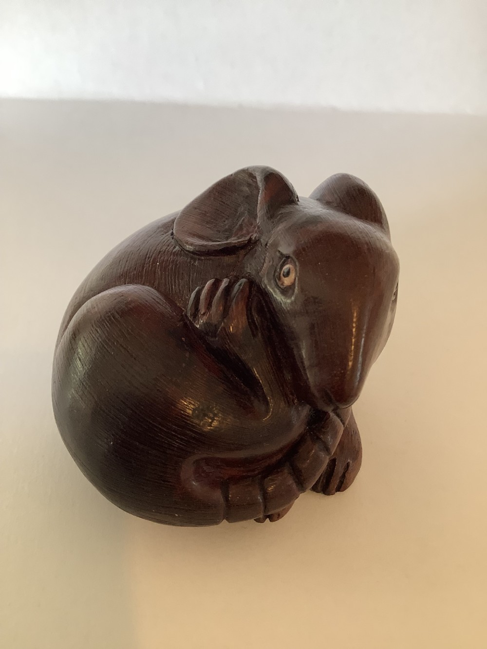 A small dark brown carved wooden okimono depicting a curled rodent with hair texture and inlaid eyes.