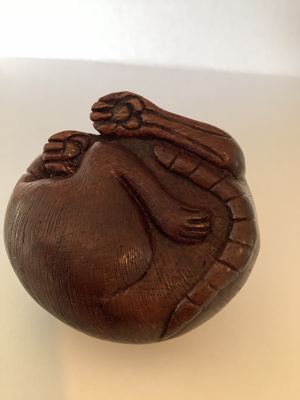 A small dark brown carved wooden okimono depicting a curled rodent with hair texture and inlaid eyes. View II