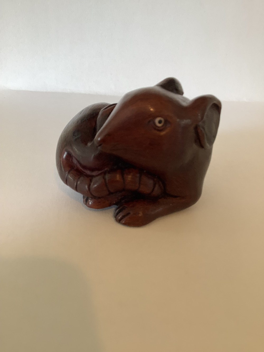 A small dark brown carved wooden okimono depicting a curled rodent with hair texture and inlaid eyes. View V