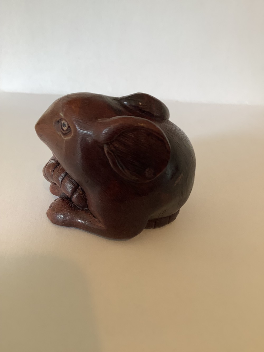 A small dark brown carved wooden okimono depicting a curled rodent with hair texture and inlaid eyes. View VI