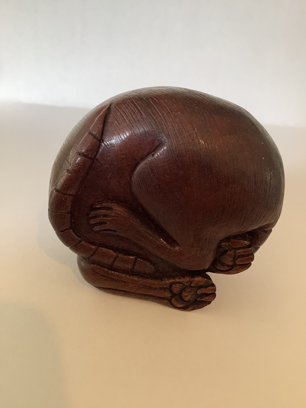 A small dark brown carved wooden okimono depicting a curled rodent with hair texture and inlaid eyes. View VII