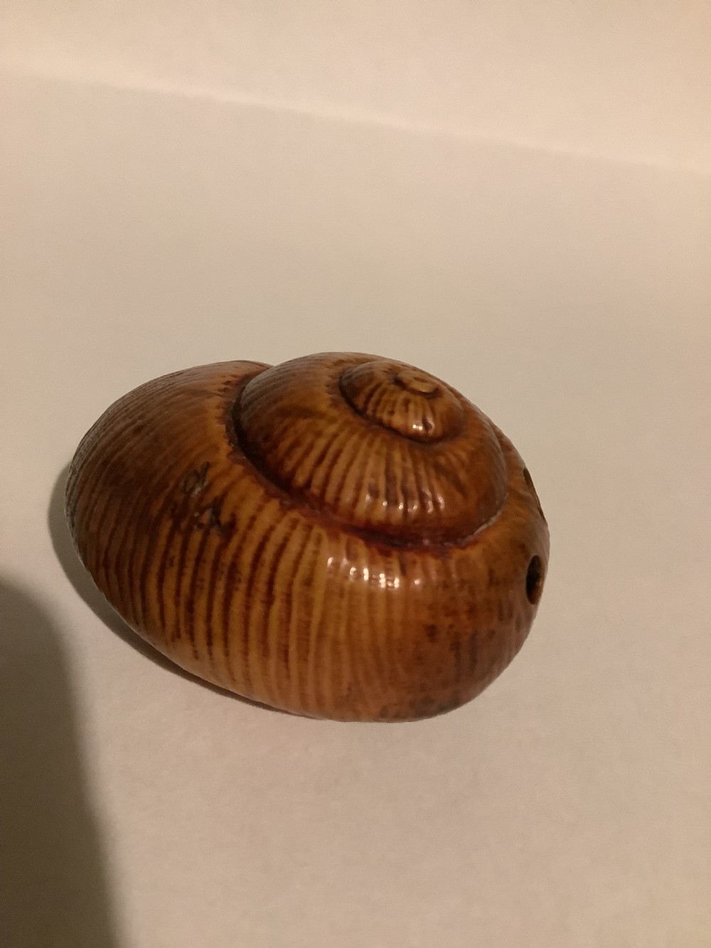 A small Japanese carved wooden netsuke depicting a frog resting on a spiralled shell. View II