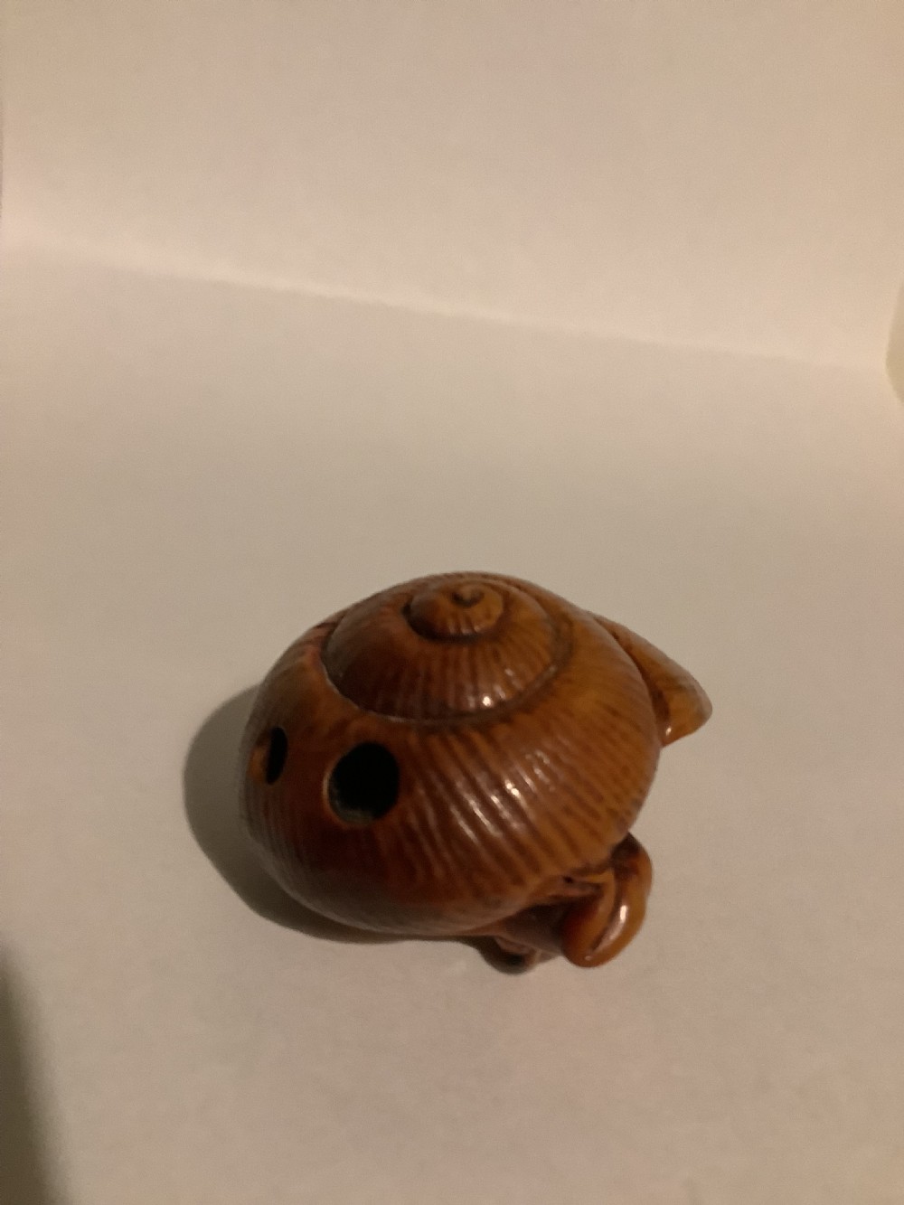 A small Japanese carved wooden netsuke depicting a frog resting on a spiralled shell. View IV
