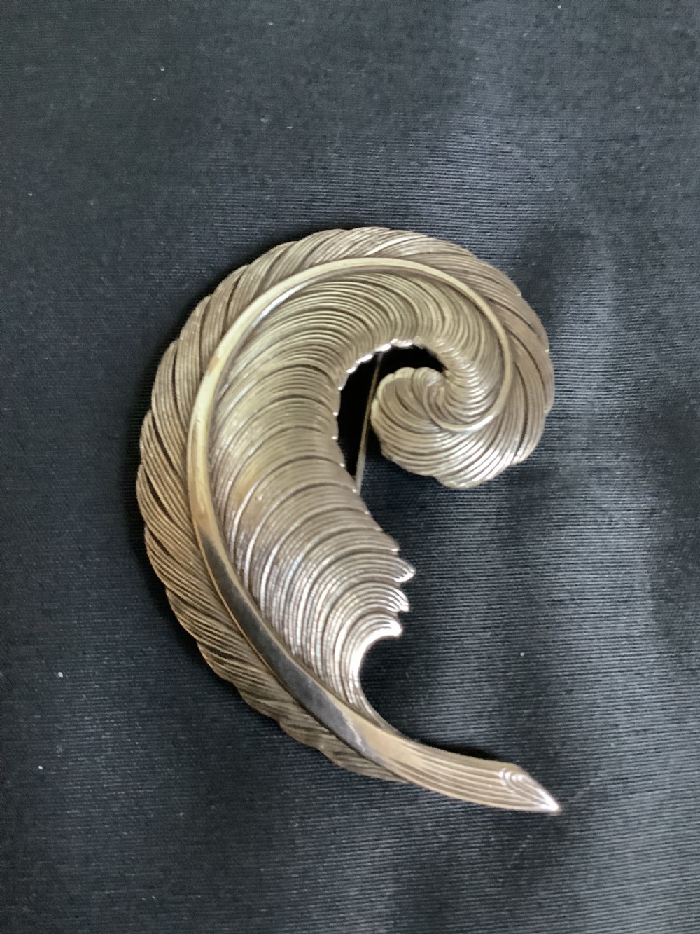 A curved white metal brooch designed in the shape of a textured feather plume with a pin fastening on the reverse. View IV