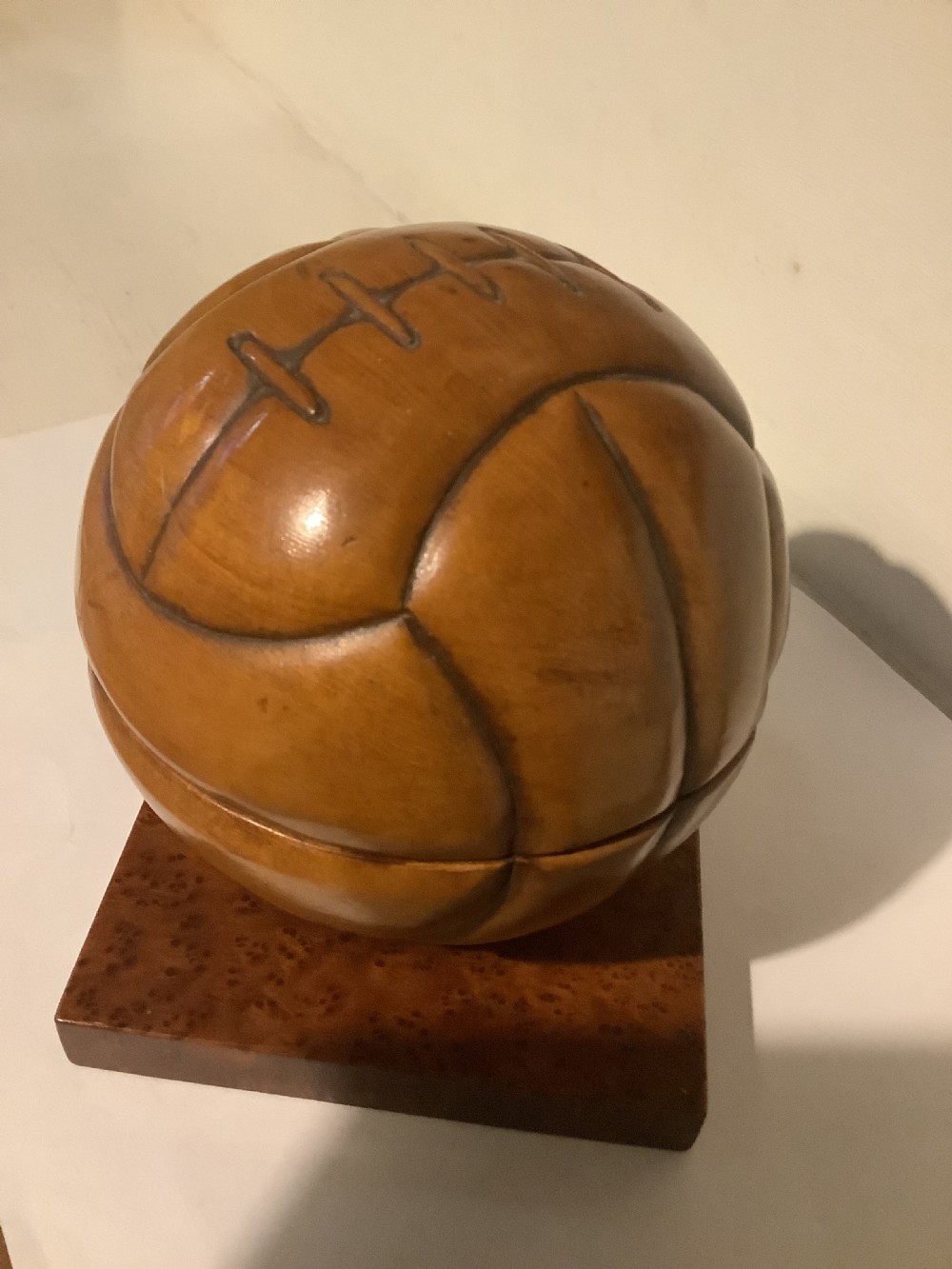 A carved hardwood lidded box shaped like a vintage laced football, mounted on a square burr wood base. View IV