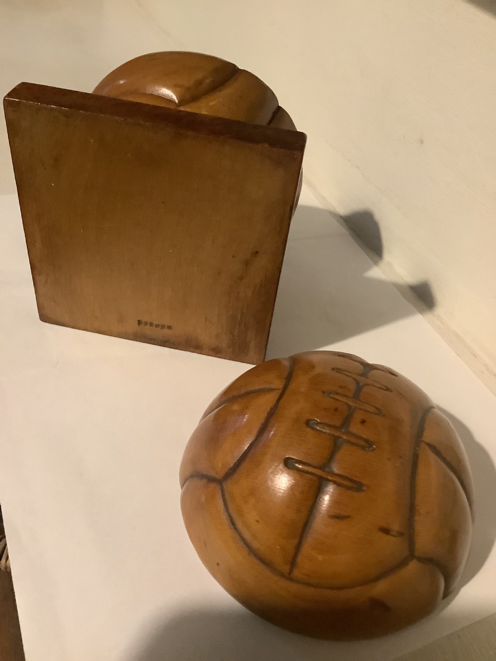 A carved hardwood lidded box shaped like a vintage laced football, mounted on a square burr wood base. View VII