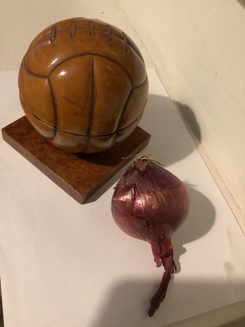 A carved hardwood lidded box shaped like a vintage laced football, mounted on a square burr wood base. View VIII