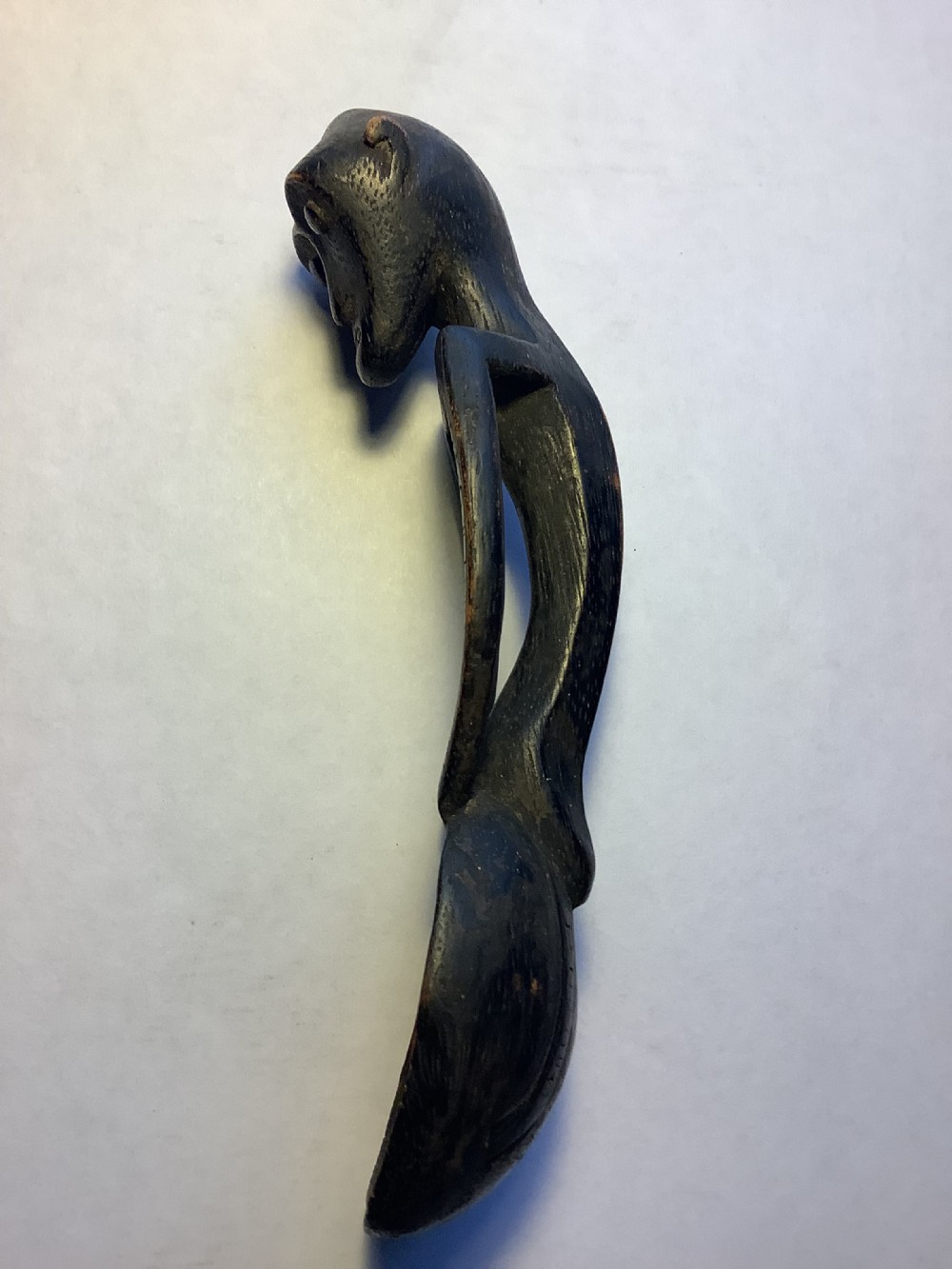 A dark carved wooden spoon featuring a handle sculpted into a stylized human figure with incised geometric markings along the arms. View III