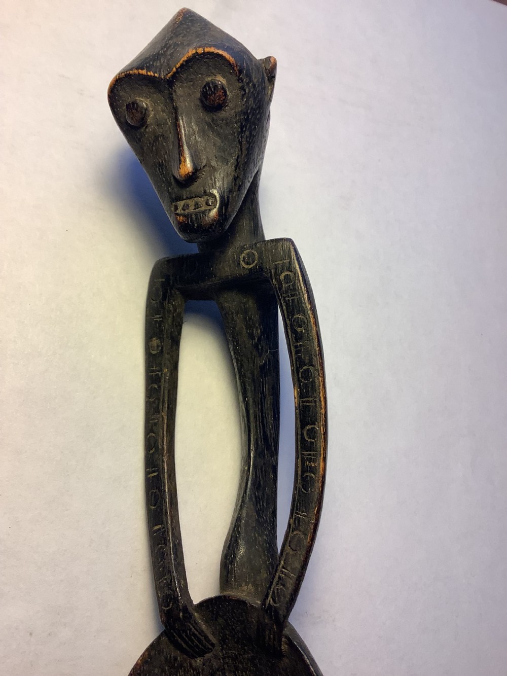 A dark carved wooden spoon featuring a handle sculpted into a stylized human figure with incised geometric markings along the arms. View IV