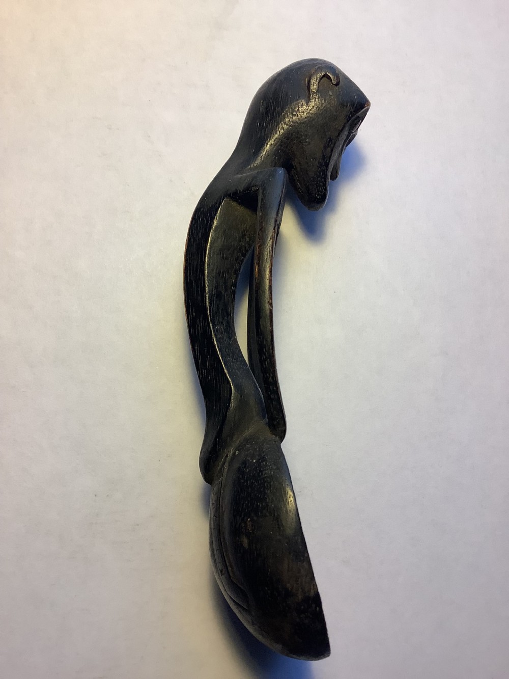 A dark carved wooden spoon featuring a handle sculpted into a stylized human figure with incised geometric markings along the arms. View V